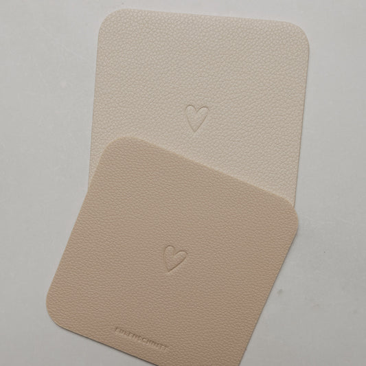 Zwei quadratische Untersetzer in Creme und Beige mit abgerundeten Ecken und geprägtem Herz