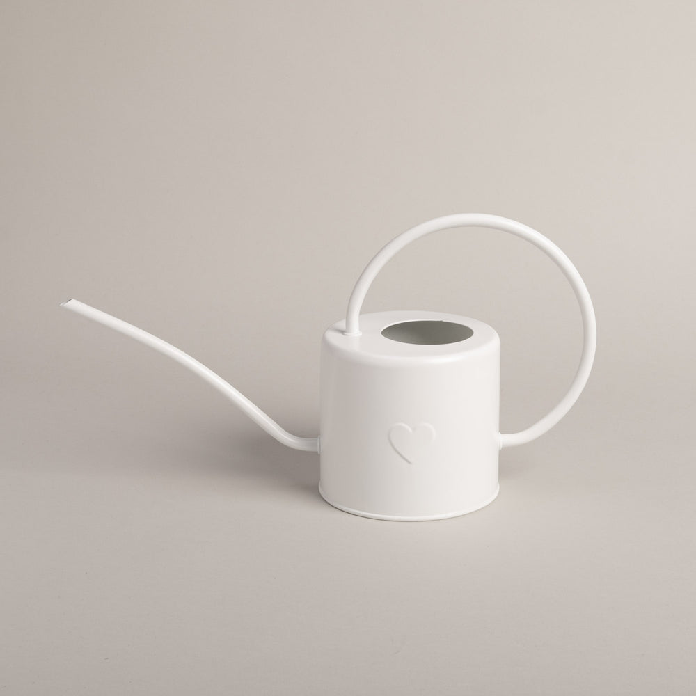 Weiße Gießkanne aus Metall mit Herzprägung, seitlich fotografiert vor hellem Hintergrund