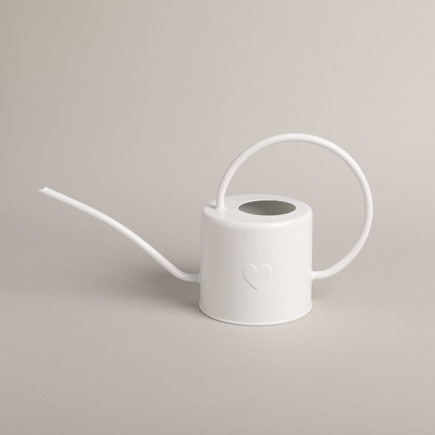 Weiße Gießkanne aus Metall mit Herzprägung, seitlich fotografiert vor hellem Hintergrund