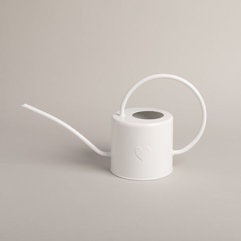 Weiße Gießkanne aus Metall mit Herzprägung, seitlich fotografiert vor hellem Hintergrund