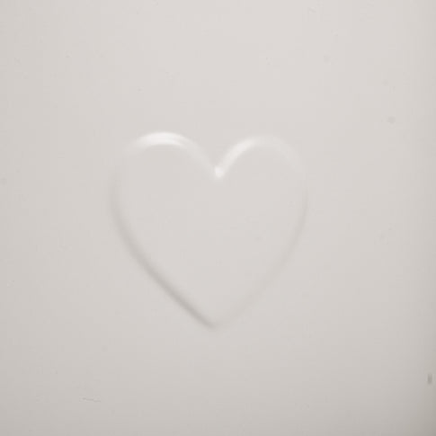 Herzprägung im Detail auf der glatten Oberfläche der weißen Metallgießkanne