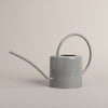 Graue Gießkanne aus Metall mit Herzdetail, seitlich fotografiert – stilvolles Accessoire für Haus und Garten.