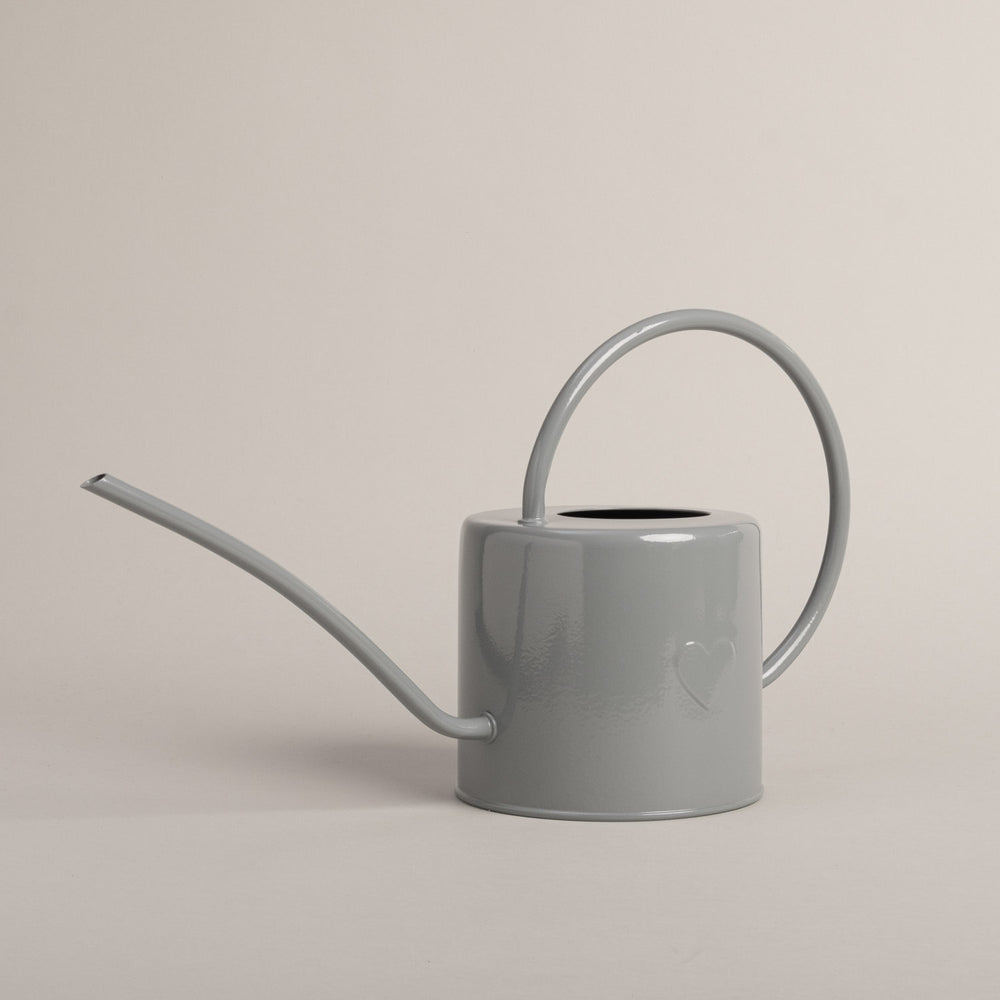 Graue Gießkanne aus Metall mit Herzdetail, seitlich fotografiert – stilvolles Accessoire für Haus und Garten.