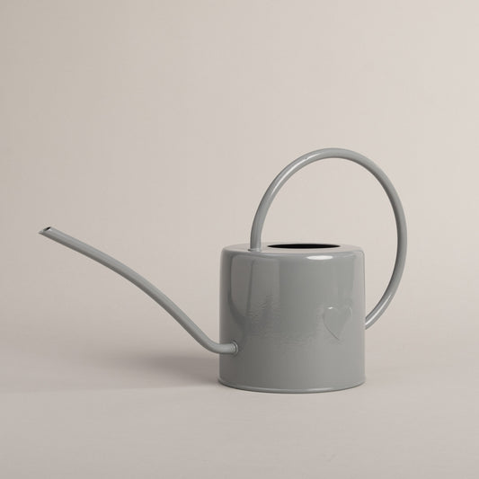 Graue Gießkanne aus Metall mit Herzdetail, seitlich fotografiert – stilvolles Accessoire für Haus und Garten.