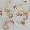 ABC Schlüsselanhänger in der Farbe rosa liegen verstreut auf einem Tisch. Einige mit der Vorderseite und einige mit der Hinterseite, die gold matt ist.
