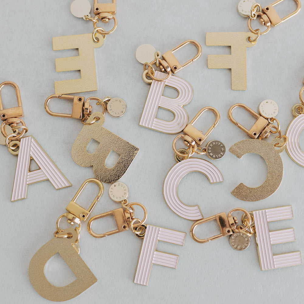 ABC Schlüsselanhänger in der Farbe rosa liegen verstreut auf einem Tisch. Einige mit der Vorderseite und einige mit der Hinterseite, die gold matt ist.