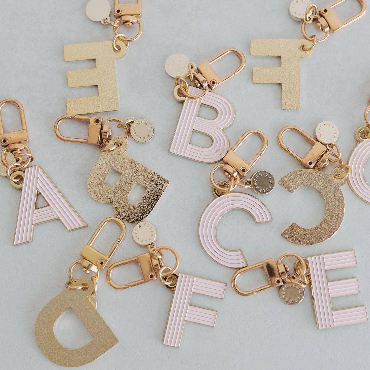 ABC Schlüsselanhänger in der Farbe rosa liegen verstreut auf einem Tisch. Einige mit der Vorderseite und einige mit der Hinterseite, die gold matt ist.