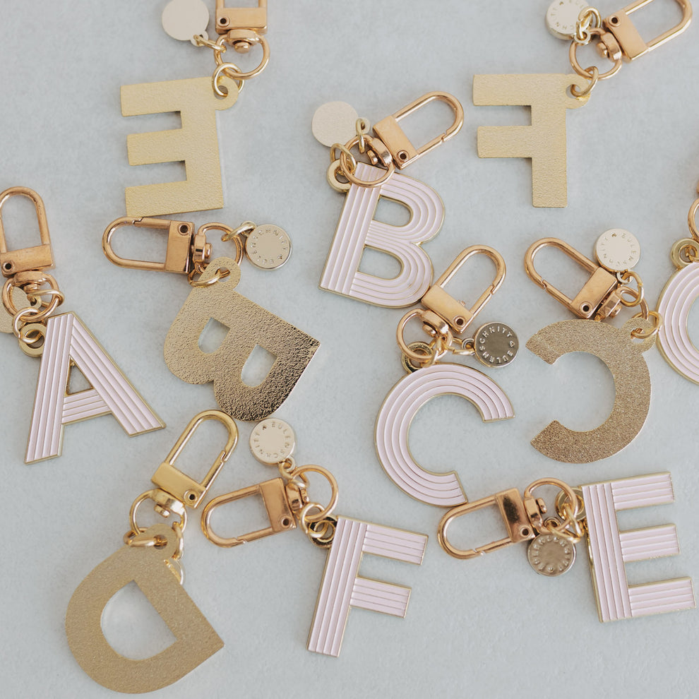 ABC Schlüsselanhänger in der Farbe rosa liegen verstreut auf einem Tisch. Einige mit der Vorderseite und einige mit der Hinterseite, die gold matt ist.