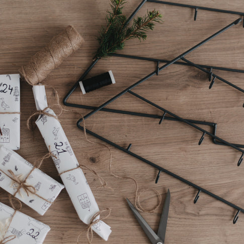 Adventskalender Tanne liegt auf Holztisch mit Bastelutensilien und Geschenkverpackungen.