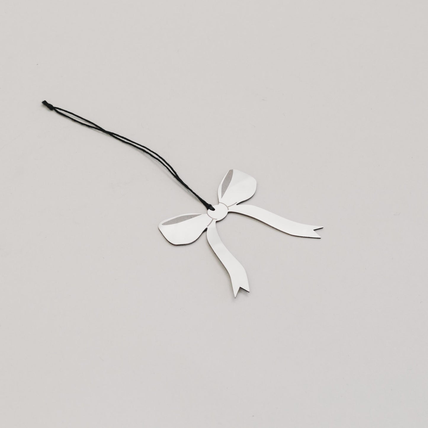 Filigraner Metallanhänger in Schleifenform liegt schräg auf hellem Untergrund, glänzend und elegant.