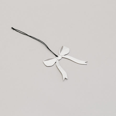 Filigraner Metallanhänger in Schleifenform liegt schräg auf hellem Untergrund, glänzend und elegant.