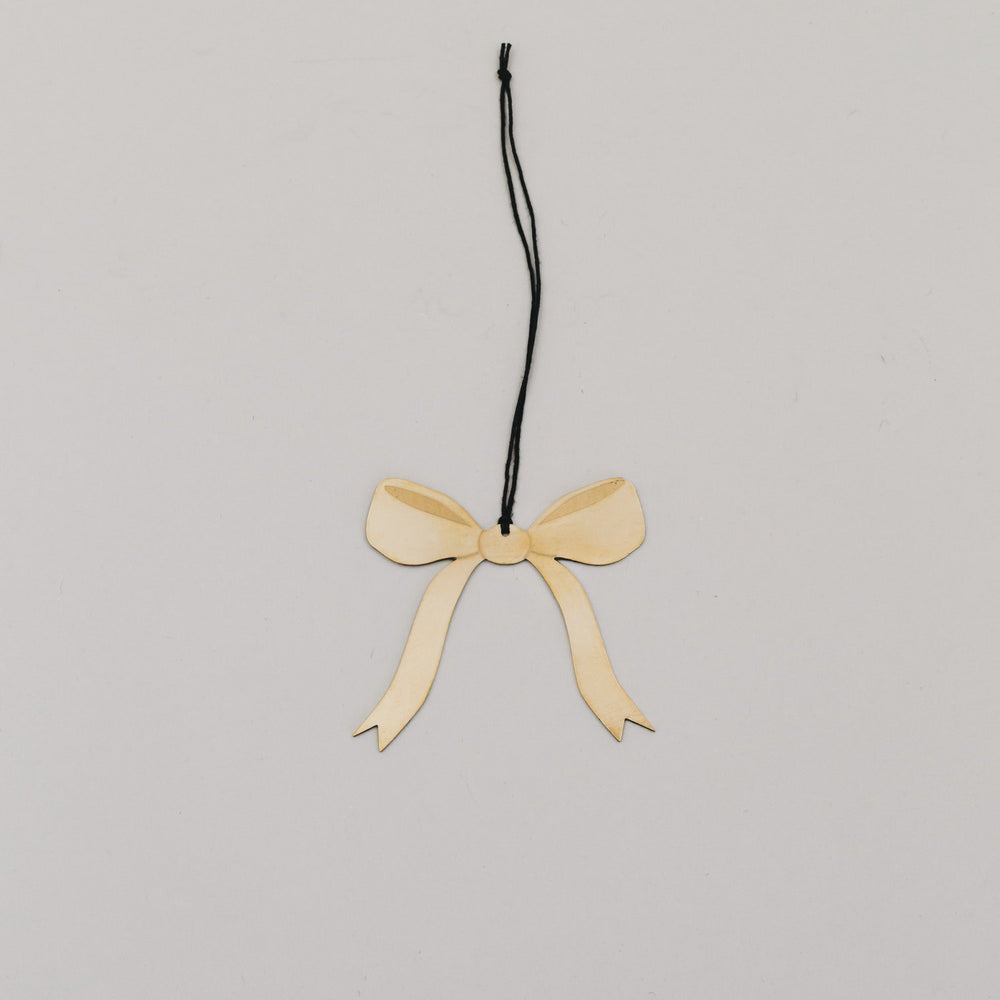 Filigraner Schleifenanhänger aus Goldmetall mit schwarzem Band auf hellem Hintergrund.