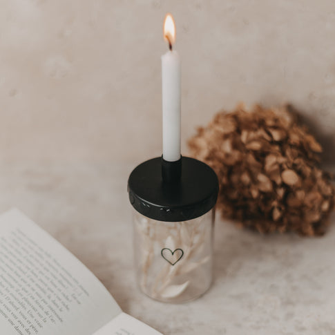 Stimmungsbild mit brennender Kerze:
Kerzenglas mit Mini-Vorratsglas, Deko und brennender Tannebaumkerze.