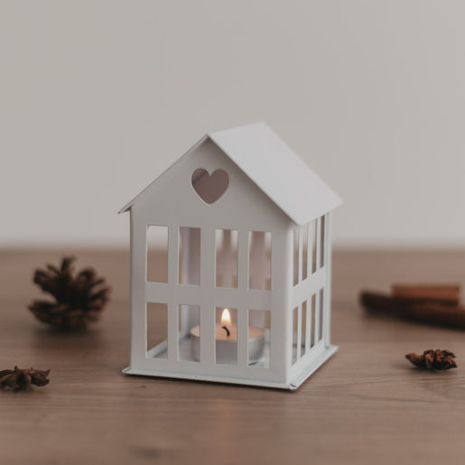Weißes Metallhaus mit Teelicht auf Holztisch, gemütliche Lichtstimmung und natürliche Dekoelemente.