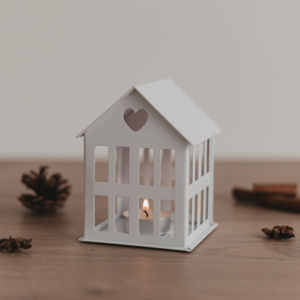 Weißes Metallhaus mit Teelicht auf Holztisch, gemütliche Lichtstimmung und natürliche Dekoelemente.