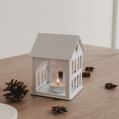 Weißes Metallhaus mit Teelicht auf Holztisch, gemütliche Lichtstimmung und natürliche Dekoelemente.