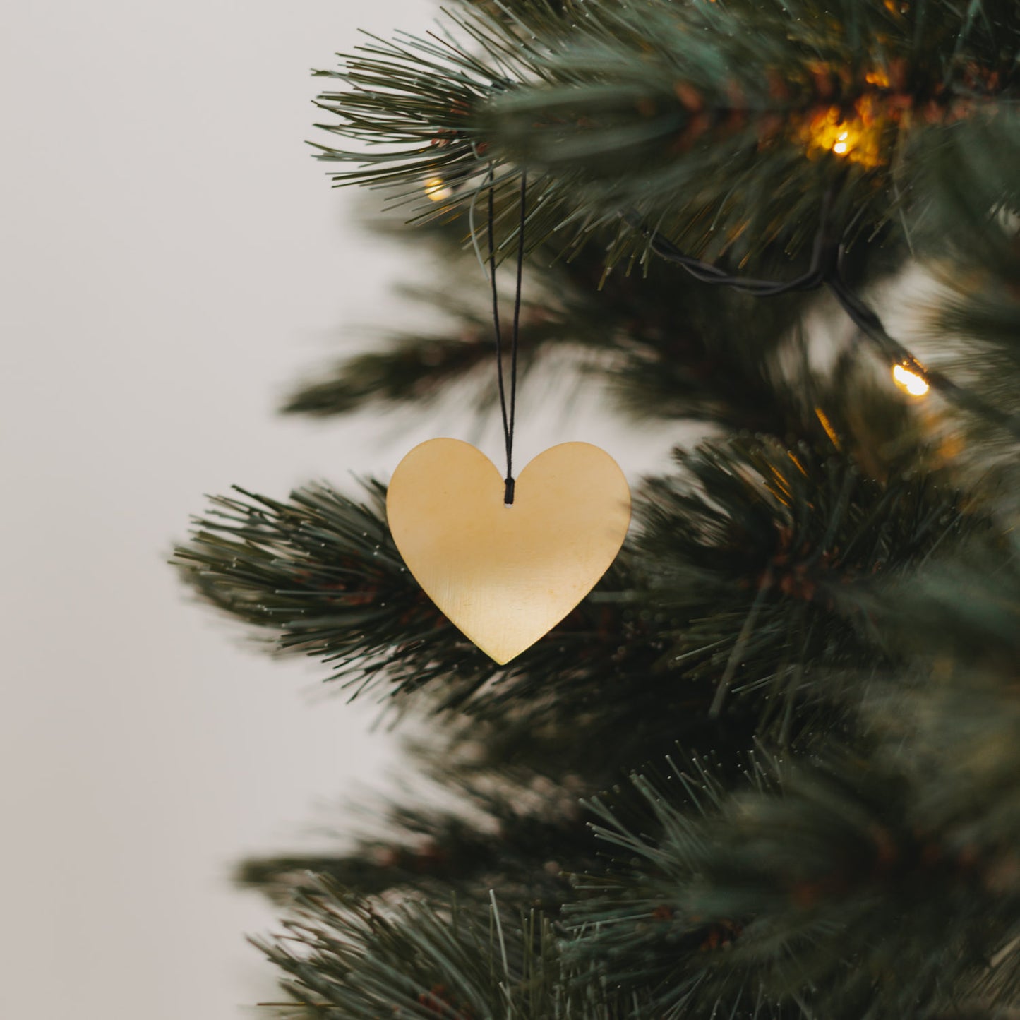 Filigraner Herzanhänger in Goldoptik am Weihnachtsbaum mit warmen Lichtern und schwarzen Aufhängeband.