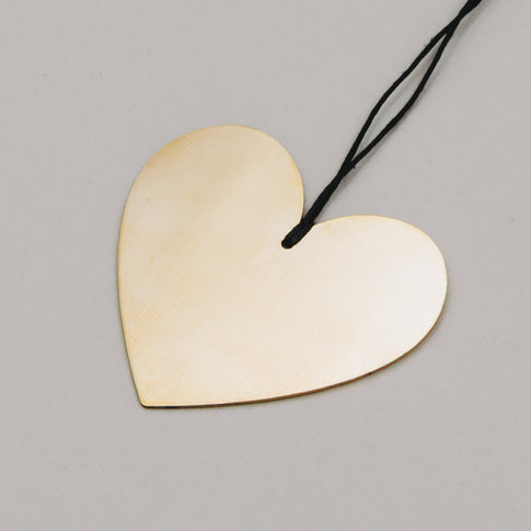 Nahaufnahme eines glänzenden Herzanhängers aus Goldmetall mit Aufhängeband in Schwarz auf grauem Hintergrund.