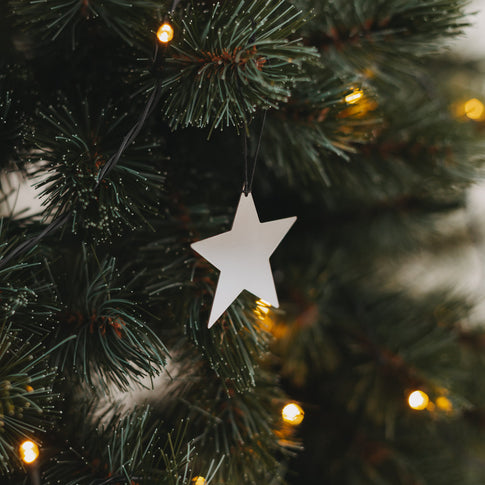 Glänzender silberner Sternanhänger am Weihnachtsbaum mit feinen Lichterketten im Hintergrund.