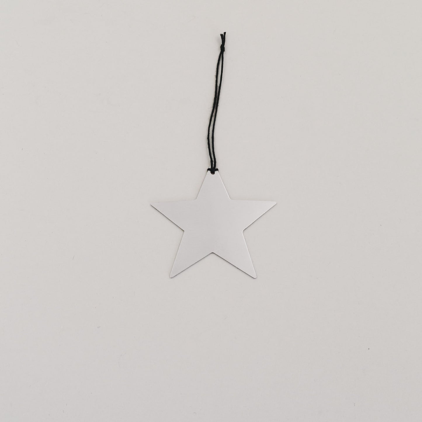 Silberner Sternanhänger aus Metall mit schwarzer Kordel auf hellem Hintergrund, minimalistisch arrangiert.
