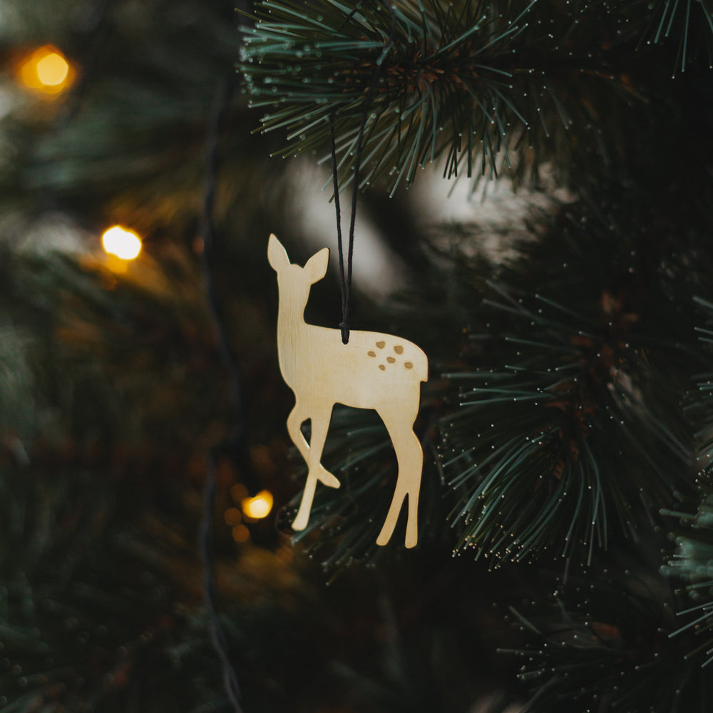 Goldener Rehanhänger  mit schwarzem Band an grünem Tannenzweig, umgeben von warmem Lichterglanz.