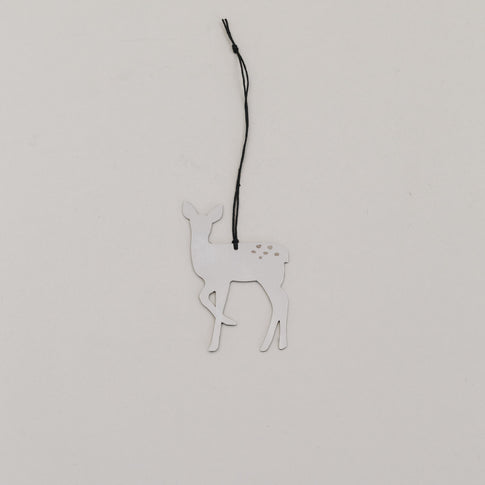 Silberner Rehnhänger aus Metall mit schwarzer Kordel auf hellem Hintergrund, minimalistisch arrangiert.