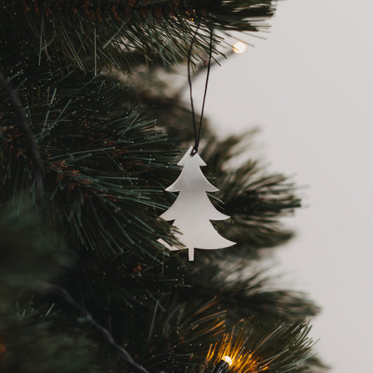 Silberner Tannenanhänger  mit schwarzem Band an grünem Tannenzweig.