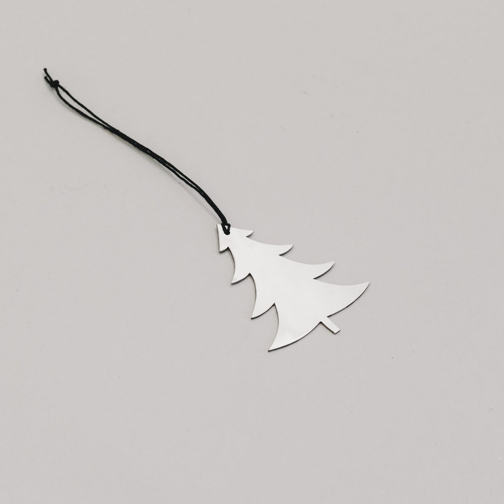 Schlichter silberner Tannenanhänger aus Metall mit schwarzem Band, auf hellem Untergrund liegend.