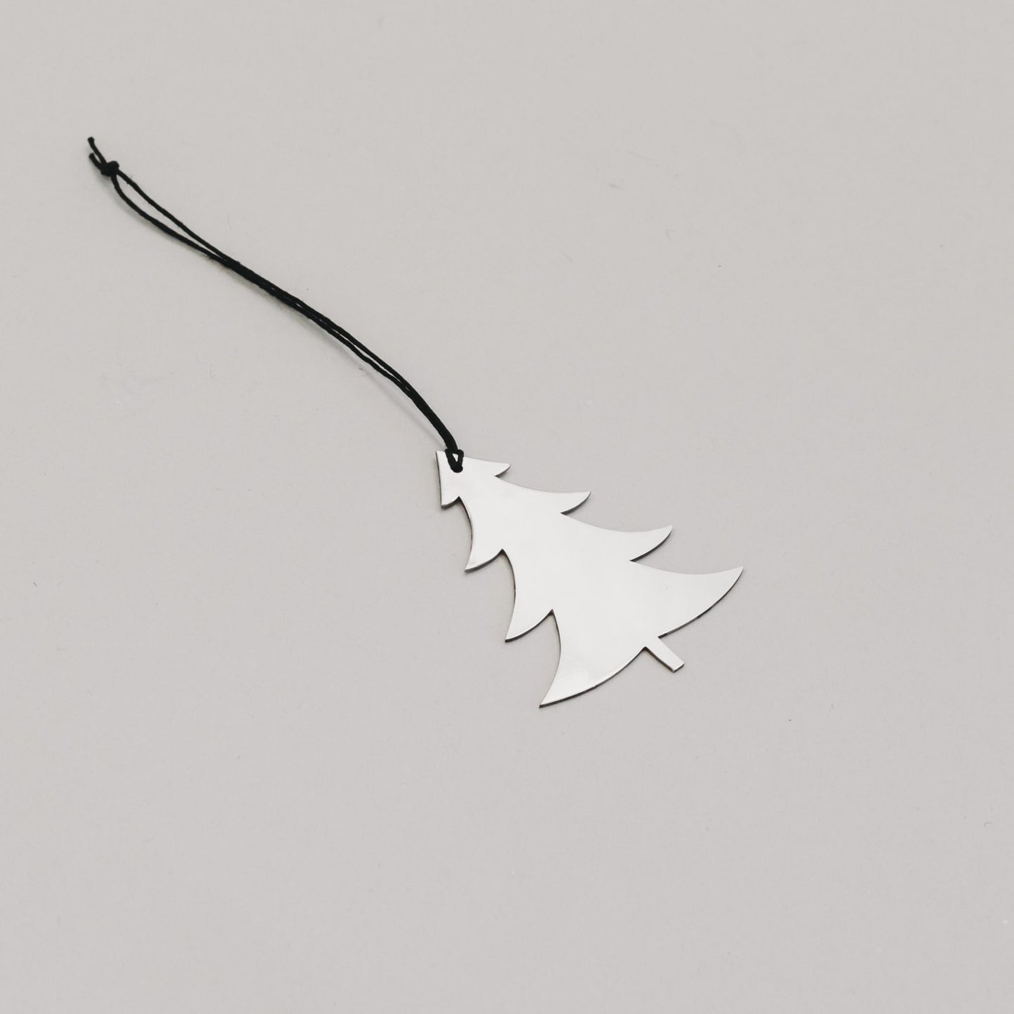 Schlichter silberner Tannenanhänger aus Metall mit schwarzem Band, auf hellem Untergrund liegend.