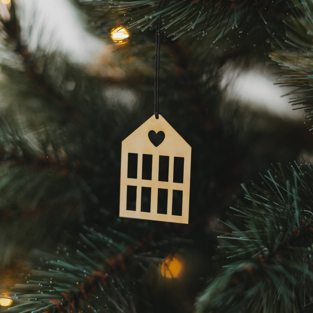 Goldener Hausanhänger  mit schwarzem Band an grünem Tannenzweig.