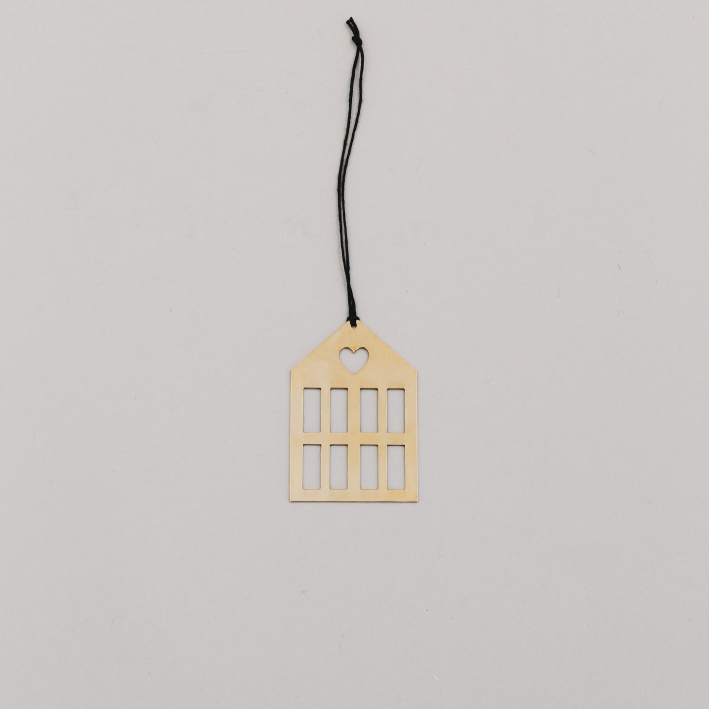 Goldener Hausanhänger aus Metall mit schwarzer Kordel auf hellem Hintergrund, minimalistisch arrangiert.