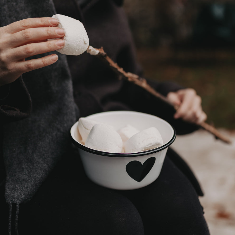 Person hält Emaille Schale Herz mit Marshmallows – perfekt für gemütliche Momente am Lagerfeuer.