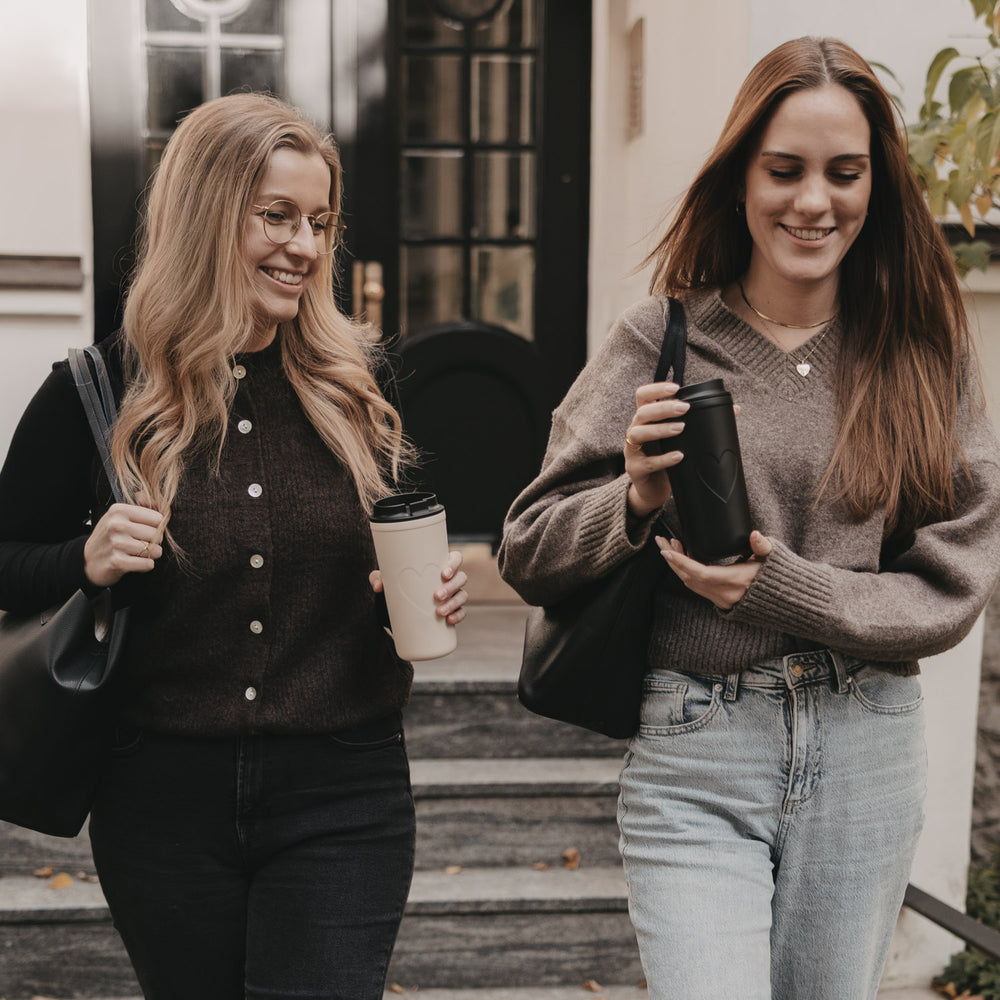 Zwei Frauen mit Eulenschnitt To-go Bechern unterwegs, nachhaltige Becher mit Herzmotiv.