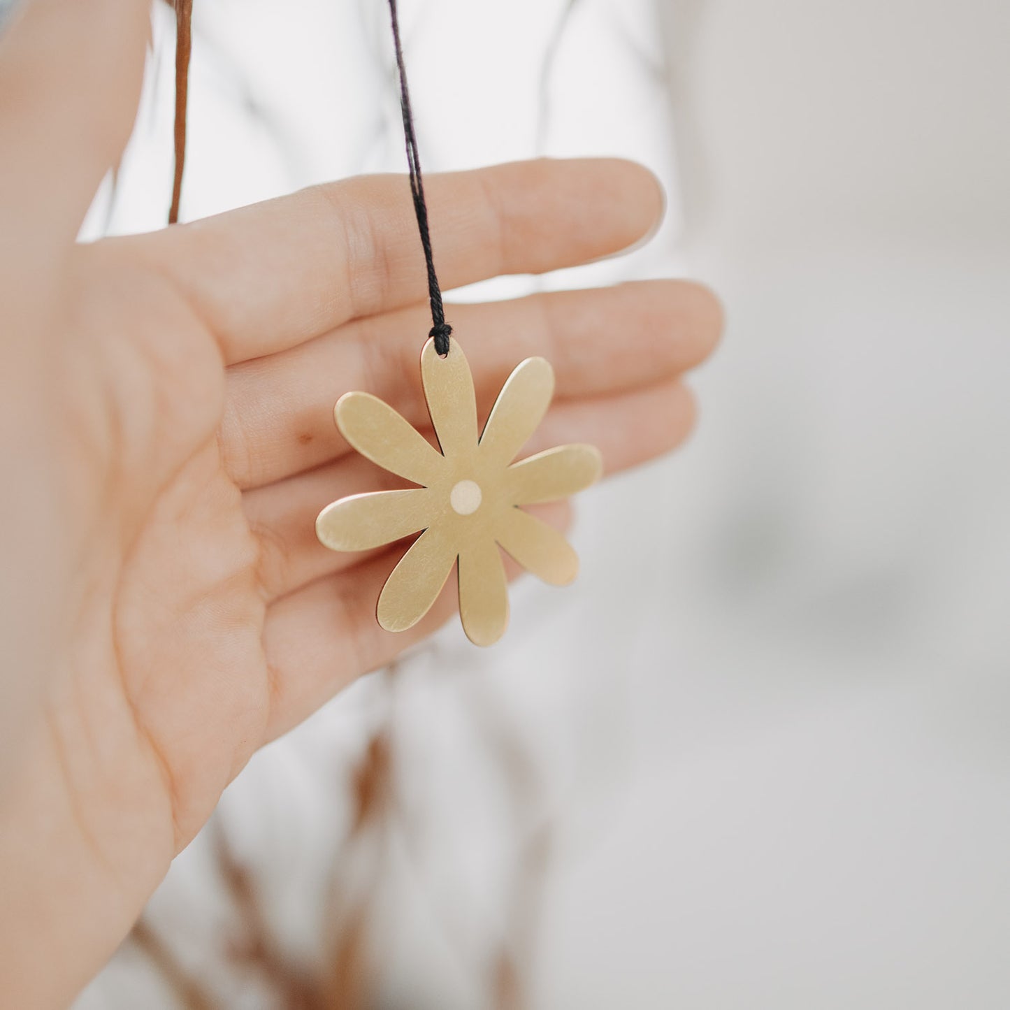 Goldener Metallanhänger Blume in der Hand – filigrane Osterdekoration.