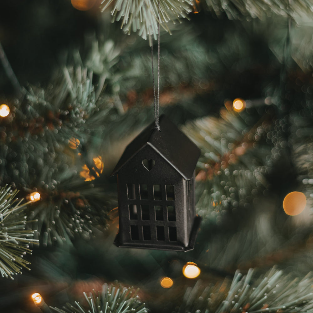 Schwarzer Metallanhänger in Hausform mit Herzdetail und Kordel am beleuchteten Weihnachtsbaum