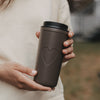 Brauner To-go-Thermobecher mit großem Herzmotiv in den Händen