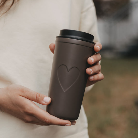 Brauner To-go-Thermobecher mit großem Herzmotiv in den Händen