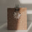Schwarzer Herz-Clip hält eine braune Geschenktüte mit Tannenbaummuster und weißem Papierstern zusammen.
