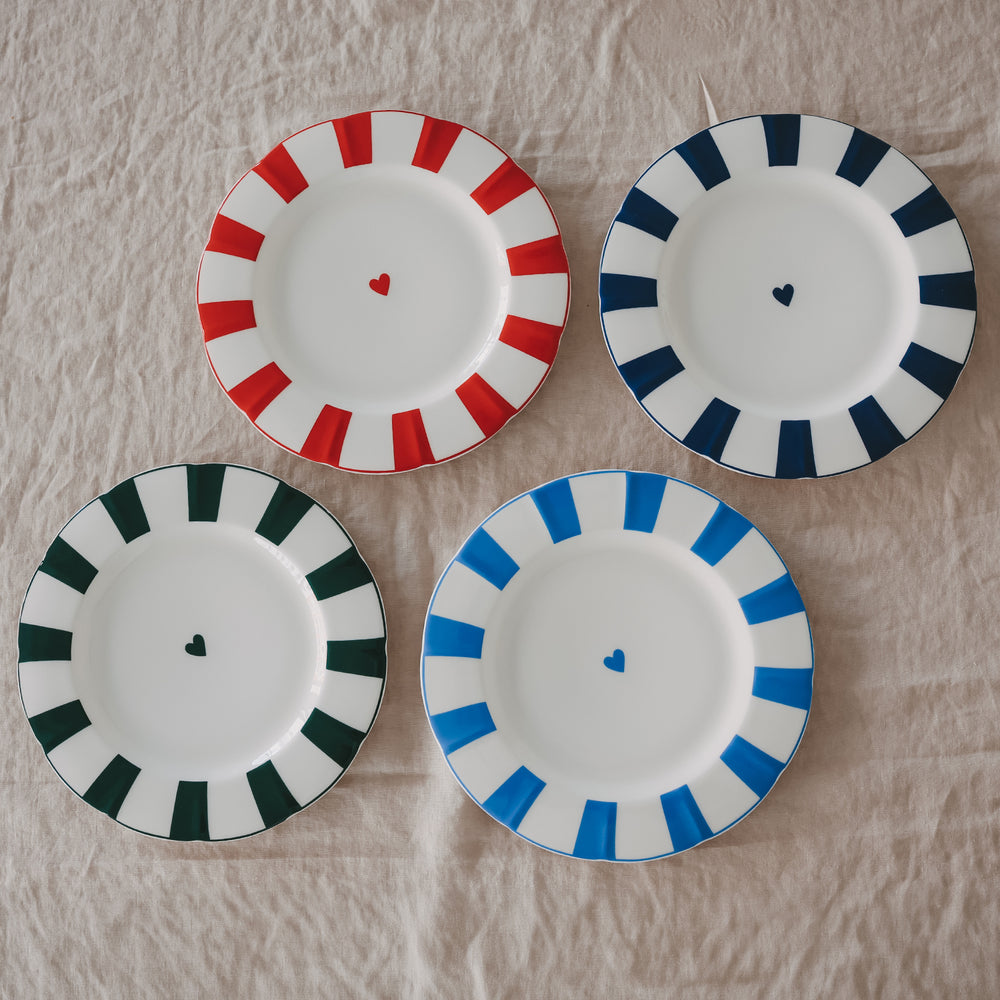 4 Porzellanteller in rot, dunkelblau, hellblau und grün mit gewelltem Rand, Streifenmuster und kleinem Herz in der Mitte auf Leinentischdecke.