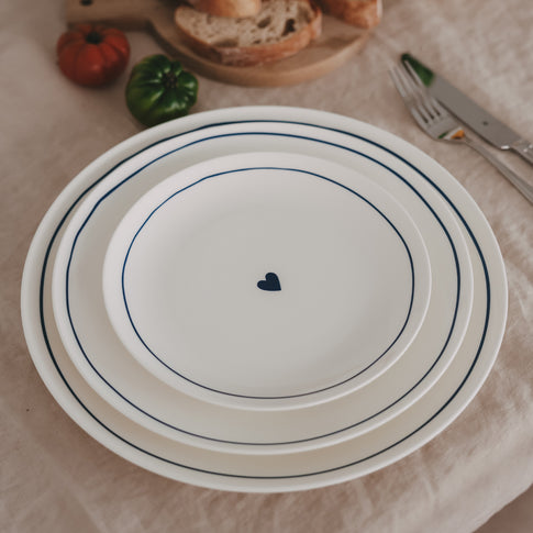 Set aus mehreren runden Tellern mit dunkelblauem Rand und Herzmotiv in verschiedenen Größen auf hellem Leinentuch angerichtet.