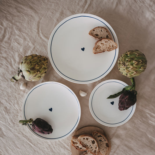 Gedeckter Tisch mit Porzellantellern mit dunkelblauem Rand und Herz, umgeben von Artischocken und Brot.