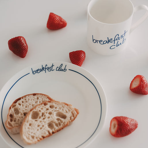Detailaufnahme eines „breakfast club“-Tellers mit dunkelblauem Rand, belegt mit zwei Brotscheiben, daneben Erdbeeren und eine passende Tasse.