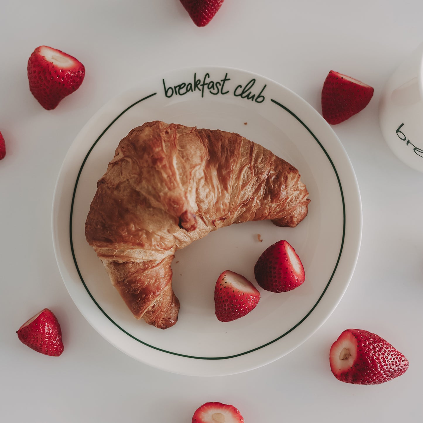 Weißer Frühstücksteller „breakfast club“ mit Croissant und frischen Erdbeeren auf hellem Hintergrund