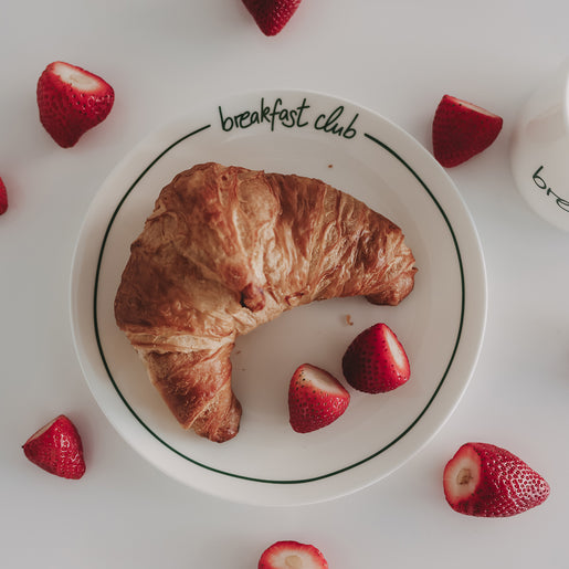 Weißer Frühstücksteller „breakfast club“ mit Croissant und frischen Erdbeeren auf hellem Hintergrund