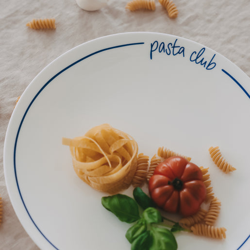 Speiseteller „pasta club“ mit dunkelblauem Rand, angerichtet mit Pasta, Tomate und Basilikum auf hellem Leinentisch.