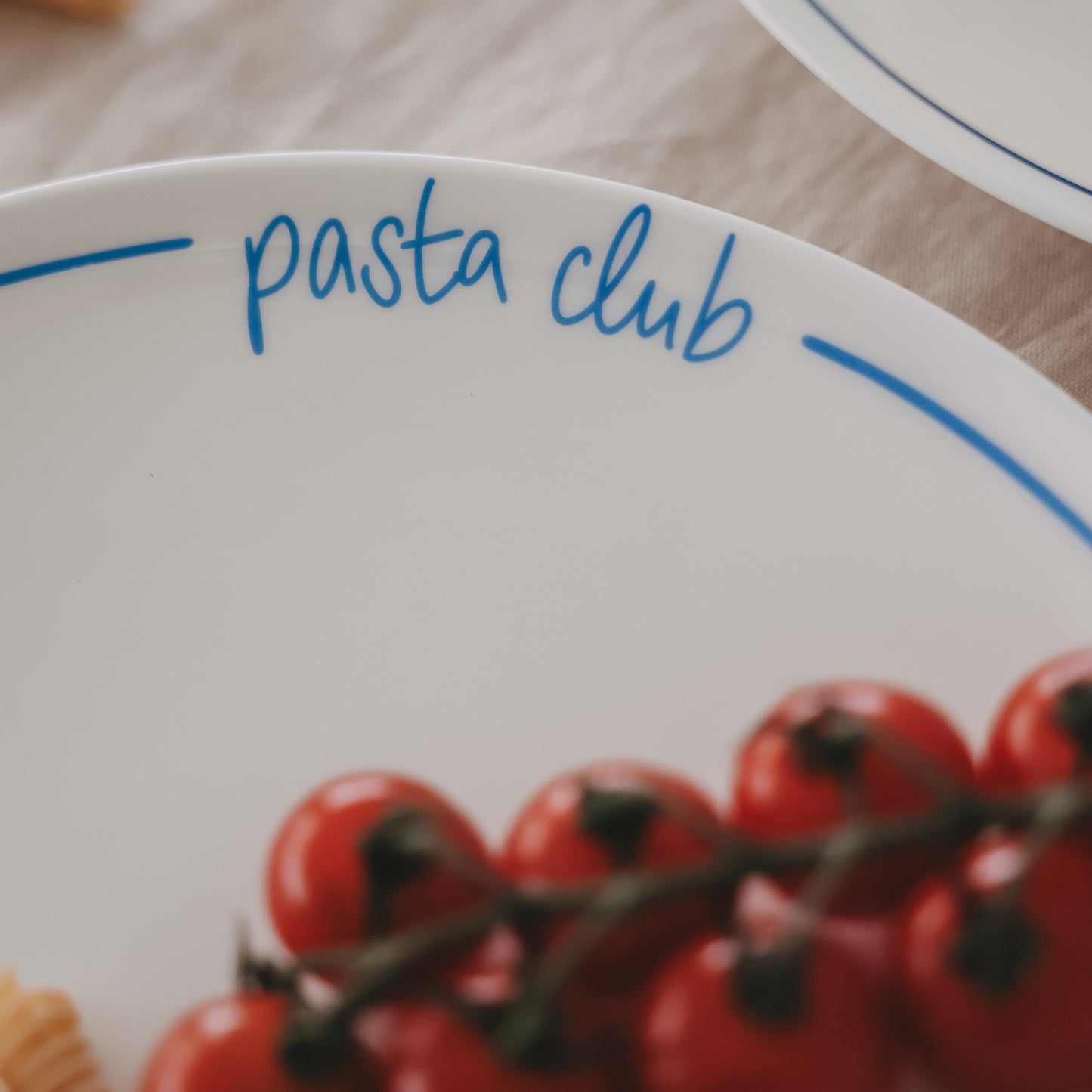 Detailaufnahme des Schriftzugs „pasta club“ auf einem weißen Speiseteller mit hellblauem Rand.