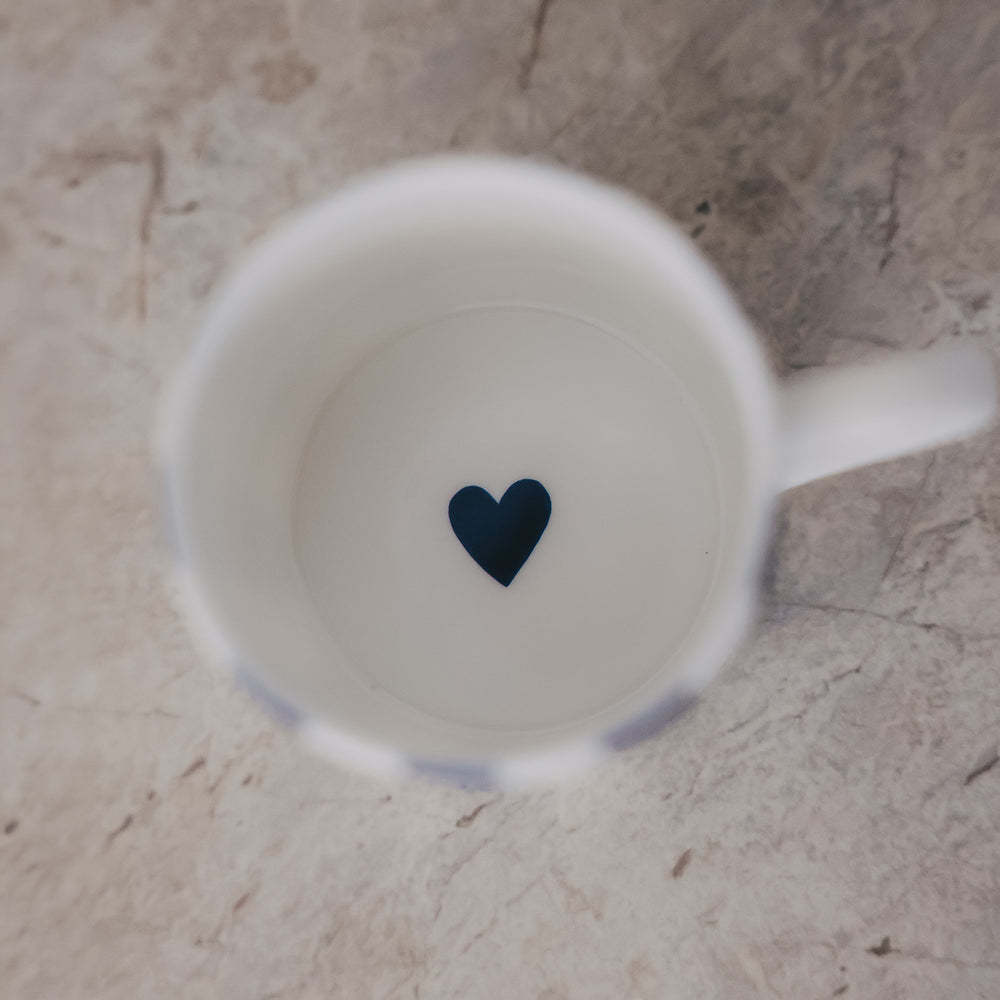 Blick in eine Tasse mit schlichtem weißem Inneren und kleinem dunkelblauen Herz am Boden.