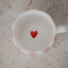 Blick in die Tasse mit weißem Inneren und kleinem rotem Herz am Boden, auf heller Steinoberfläche.