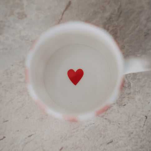 Blick in die Tasse mit weißem Inneren und kleinem rotem Herz am Boden, auf heller Steinoberfläche.