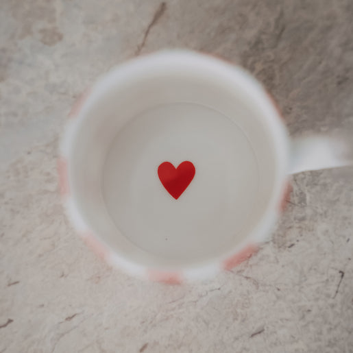 Blick in die Tasse mit weißem Inneren und kleinem rotem Herz am Boden, auf heller Steinoberfläche.